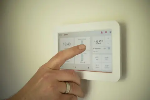 Palec dotyka ekranu termostatu, sprawdzając, ile prądu zużywa 4 osobowa rodzina miesięcznie.