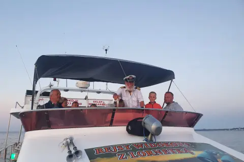 Kapitan z lornetką na pokładzie łodzi zaprasza na rejsy statkiem we Władysławowie. Rodzina cieszy się widokiem.