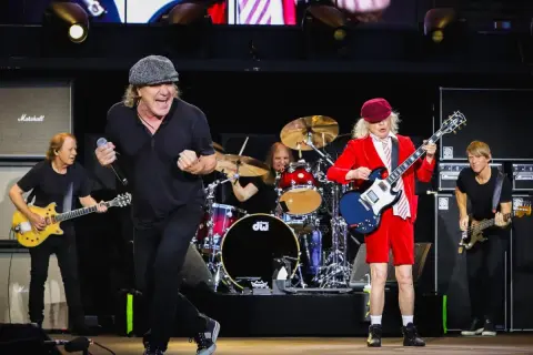Zespół AC/DC na scenie, grający swoje kultowe utwory. Wokalista w czapce, gitarzysta w czerwonym stroju.