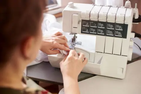 Kobieta używa maszyny do obrębiania brzegów tkaniny, tworząc delikatne wykończenie.