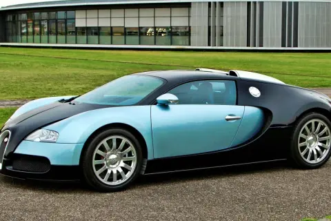 Błękitno-czarny Bugatti Veyron na tle nowoczesnego budynku i zielonego trawnika.