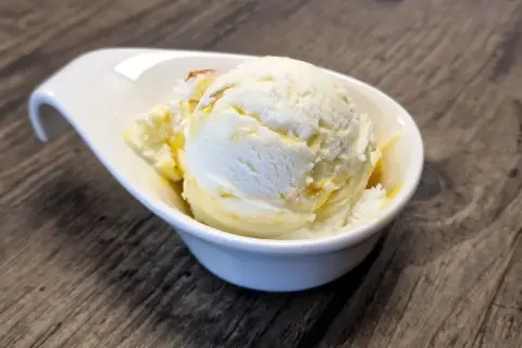 Ein cremiges Eis, das nach Buttermilch schmeckt, in einer weißen Schale auf Holztisch.