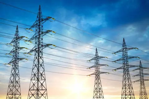 Wieże energetyczne na tle zachodzącego słońca, symbolizujące maksymalne napięcie w sieci.