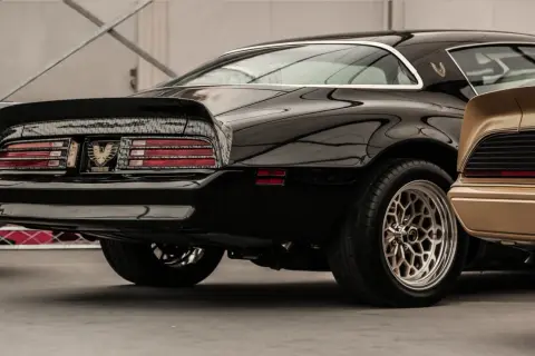 Błyszczący czarny muscle car z charakterystycznym spojlerem i felgami. Obok złoty klasyk.