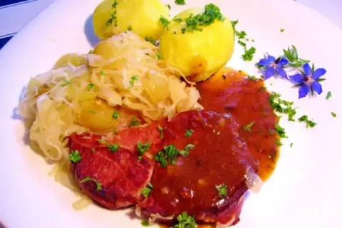 Gekochte Rippchen zubereiten: Herzhaftes Gericht mit deftigen Rippchen, Sauerkraut und Kartoffeln, garniert mit Petersilie und blauen Blüten.