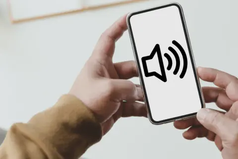 Dłoń trzyma smartfon z ikoną głośnika. Dowiedz się, jak wyłączyć dźwięk klawiszy Samsung, by pisać ciszej.