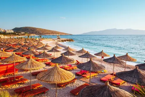 Słoneczna plaża w Albanii w lipcu, pełna parasoli i leżaków, zaprasza do odpoczynku nad turkusowym morzem.