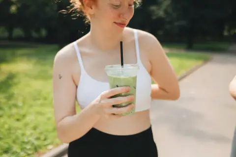 Une jeune femme aux taches de rousseur tient une boisson verte glacée, un rituel quotidien pour elle : boire du matcha.
