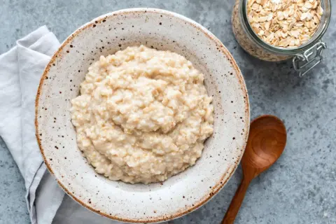 Cremiger Haferbrei in einer Schale, daneben ein Glas Haferflocken. Ein einfaches Porridge Rezept für einen gesunden Start.