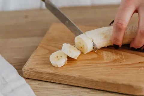 Eine Hand schneidet eine Banane in Scheiben auf einem Holzbrett. Perfekte Energie für das Training.