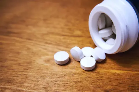 Vita tabletter, medicin mot panikångest, ligger utspridda på ett träbord bredvid en vit burk.