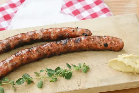 Zwei gegrillte Wildbratwürste auf einem Holzbrett mit Senf und Kräutern. Das beste Wildbratwurst Rezept für einen besonderen Genuss.