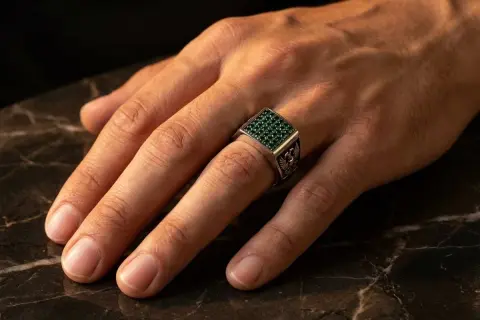 Anillo de plata con piedras verdes, puesto en el dedo anular, el dedo en que se pone un anillo normal.