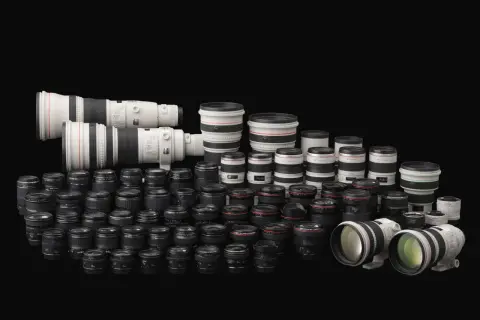 Vasta collezione di obiettivi per fotocamere, con diversi modelli e marche di macchine fotografiche, disposti su sfondo nero.