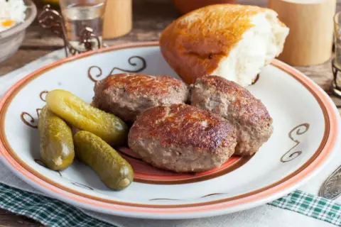 Kotlety mielone z pieczarkami, ogórki kiszone i bułka na talerzu. Pyszny, domowy obiad.