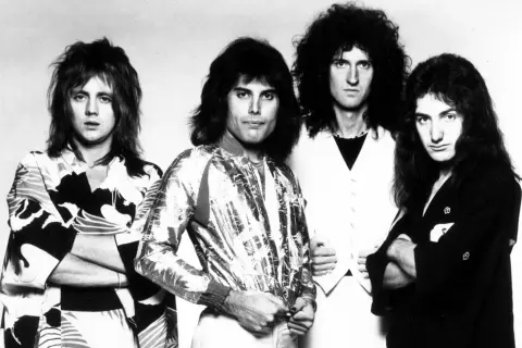 Czterech członków zespołu Queen, Freddie Mercury, Brian May, Roger Taylor i John Deacon, pozuje do zdjęcia. To oni tworzą zespół Queen, który nagrał największe hity.