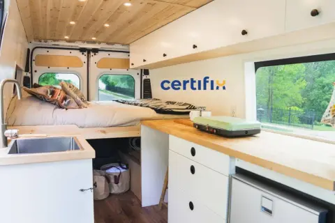 Interior de caravana con cama, fregadero y cocina. Muebles de madera y blancos, ideales para fabricantes de muebles para caravanas.