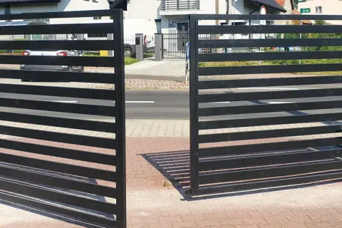 Nowoczesna, czarna brama otwierana na zewnątrz, z automatyką, stanowi eleganckie wejście na posesję.