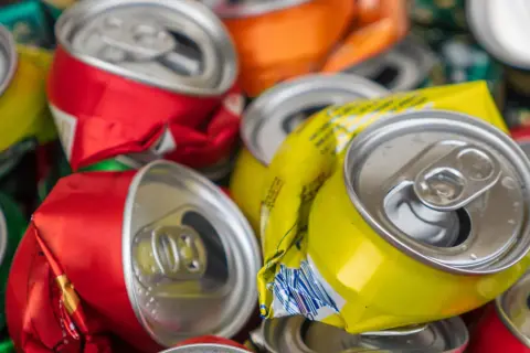Stos zgniecionych puszek aluminiowych, czerwonych, żółtych i pomarańczowych, gotowych do recyklingu.