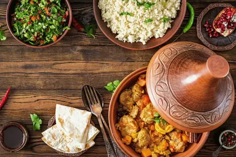 Stół z potrawami w stylu marokańskim: aromatyczny tagine z mięsem, kuskus, sałatka i chleb.
