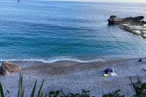 Un mare bello nel nord Italia, con un veliero all'orizzonte e persone che si godono la spiaggia di ciottoli.