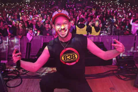 Max Pezzali sul palco, con la folla illuminata dai cellulari, indossa una maglietta con il logo 883.