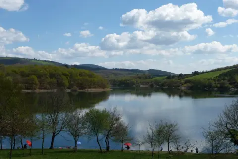 El embalse de Vilasouto, con sus aguas serenas reflejando el cielo azul y las verdes colinas, invita a disfrutar de un día tranquilo.