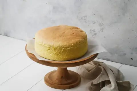 Torta soffice e dorata, preparata con albumi montati a neve, su un alzata di legno.