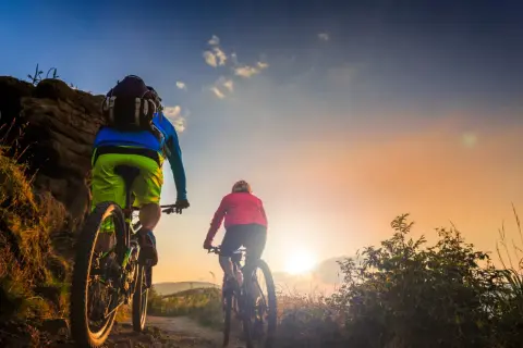Dwie osoby na rowerach górskich przemierzają malownicze **trasy velo Polska** o zachodzie słońca.