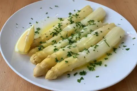 Välkokt vit sparris serverad på en vit tallrik med smält smör, hackad persilja och en citronklyfta. Enkel och god rätt!