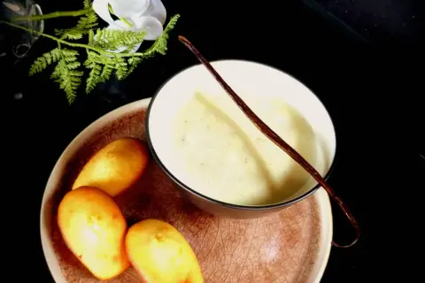 Un bol de lait vanille onctueux, garni d'une gousse de vanille, avec des madeleines dorées sur une assiette.