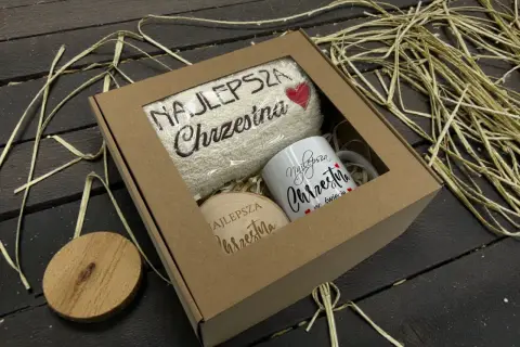 Prezent na dzień matki chrzestnej: ręcznik i kubek z napisem "Najlepsza Chrzestna", drewniany krążek.