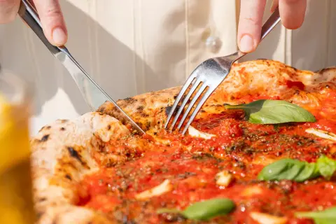 Eine Pizza Marinara wird mit Messer und Gabel angeschnitten.