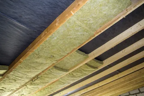 Izolacja z wełny mineralnej ułożona między drewnianymi belkami, pod czarną membraną. Czy wełna może dotykać membrany? Tak, jeśli jest to odpowiednia membrana.