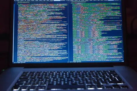 Programista pracuje nad kodem. Na ekranie laptopa widać wiele linii kodu, co pokazuje, co robi programista.