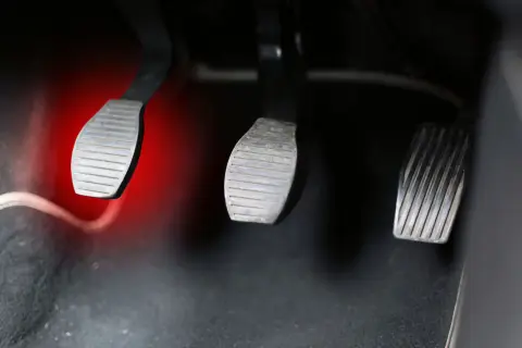 Pédales de voiture, dont celle de l'embrayage, avec une lumière rouge sur la gauche. Le **câble d'embrayage** est visible.