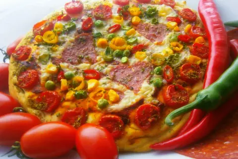 Pyszna pizza pepperoni z pomidorkami, papryką i zielonym groszkiem, otoczona świeżymi papryczkami chili i pomidorami.