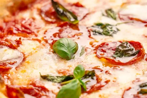 Nahaufnahme einer Pizza mit geschmolzenem Käse, roten Salami-Scheiben und frischem Basilikum. Verschiedene Salami-Sorten machen diese Pizza unwiderstehlich.