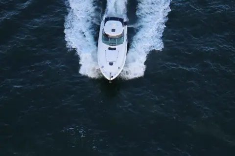 Un bianco yacht naviga veloce, lasciando una scia di spuma. La sua posizione è centrale, in un mare scuro e mosso.