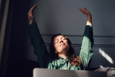 Vrouw met gesloten ogen en armen omhoog, genietend van zonlicht. Ze voelt zich eindelijk comfortabel in haar lichaam, na lang onzeker te zijn geweest.