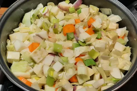 Poêlée de légumes coupés en dés, prêts pour un savoureux bouillon de légume. Carottes, poireaux et navets se mélangent.
