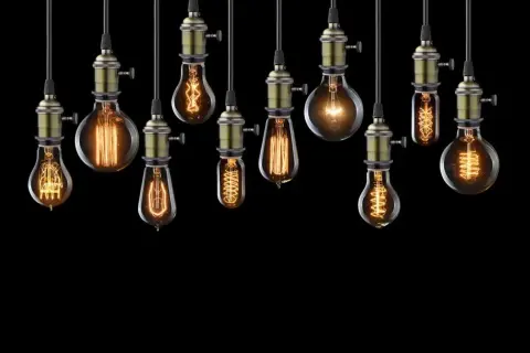 Rząd wiszących lamp w kształcie żarówki, każda z unikalnym, ozdobnym żarnikiem i mosiężnym mocowaniem, tworzy ciepłą, nostalgiczną atmosferę.