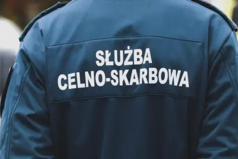 Celnik w granatowej kurtce z napisem "SŁUŻBA CELNO-SKARBOWA" stoi obok pojazdu.