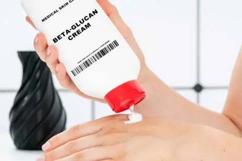 Eine Hand hält eine Tube "Beta-Glucan Cream" und gibt eine kleine Menge auf die andere Hand. Die Creme verspricht eine positive **Beta-Glucan Wirkung Haut**.
