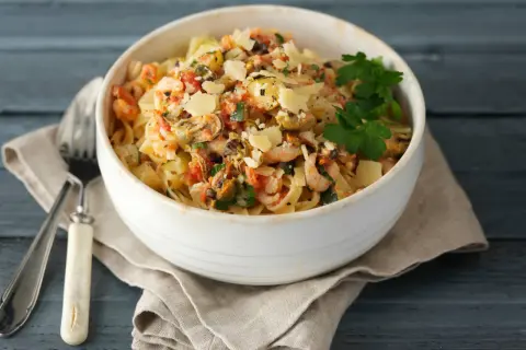 En skål med frutti di mare pasta, toppad med parmesan och persilja, serverad med en gaffel på en duk.
