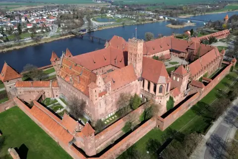 Ogromny zamek z czerwonej cegły, największy zamek w Europie, otoczony murami obronnymi, nad rzeką.
