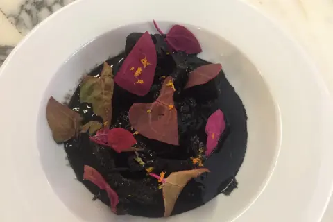 Un plat de ragout de seiche à l'encre noire, garni de pétales de fleurs séchées et d'une touche d'agrume.
