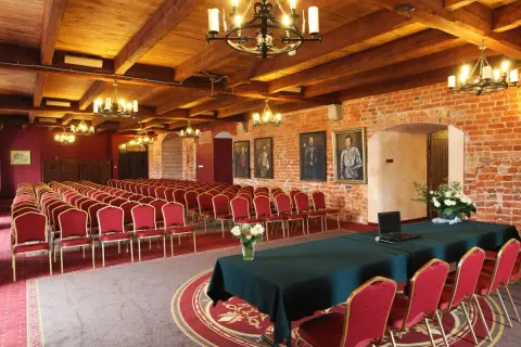 Elegancka sala konferencyjna w hotelu z **luxury collection**, z rzędami czerwonych krzeseł, drewnianym sufitem i ceglanymi ścianami.