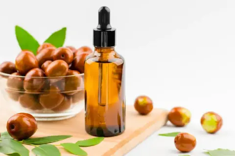 Olio di jojoba a cosa serve? Un flacone ambrato con contagocce accanto a una ciotola di frutti di jojoba e foglie verdi.