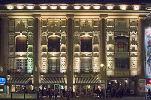 Der Admiralspalast Berlin bei Nacht, beleuchtet mit Säulen und Verzierungen. Menschen stehen vor den Eingängen und Cafés.